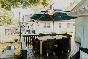 Eine Holzterrasse mit Tisch, Stühlen, Sonnenschirm und Lichterkette.
