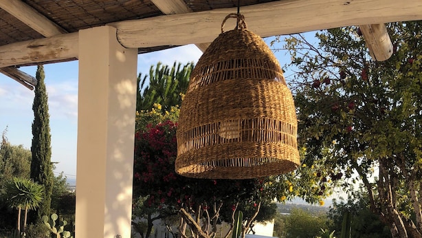 An outdoor dining area with a table set for six, a hanging wicker basket, and a view of a pool and garden.