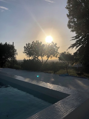 Una piscina con borde de azulejos, rodeada de árboles y un cielo despejado.