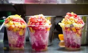Drei Plastikbecher mit Obstschichten und einer rosa Flüssigkeit, vermutlich ein Dessert oder Getränk.