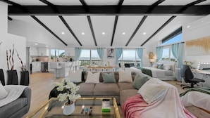 A spacious living area with a sofa, coffee table, and a view of the kitchen and balcony.