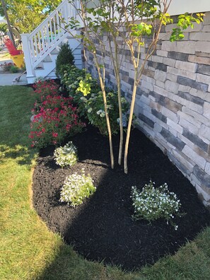 A landscaped garden with a stone wall, a white fence, and various flowering plants.