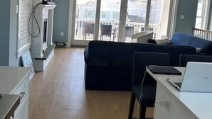 Tilava olohuone, jossa on korkea katto, kattotuuletin, suuri ikkuna ja tummanvärinen sohva.