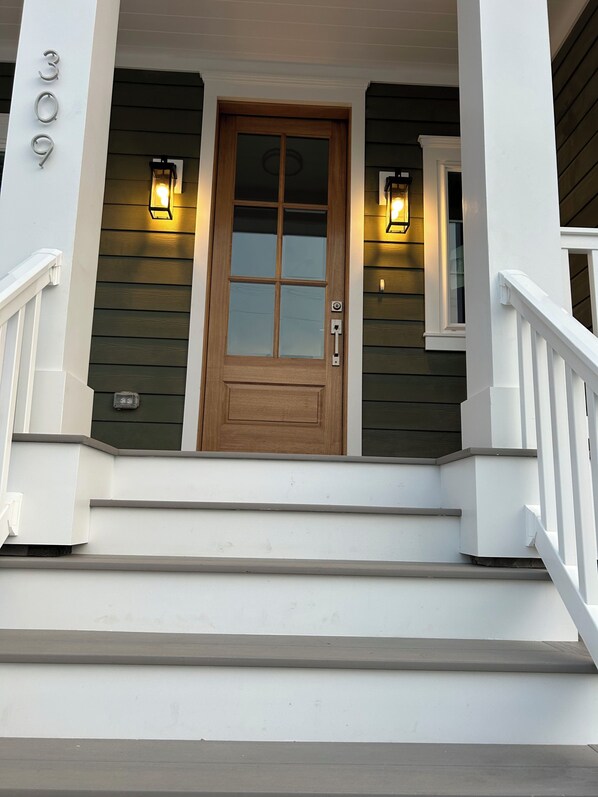 A wooden front door with a glass panel, flanked by two wall-mounted lights, and a white staircase leading to the entrance.