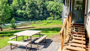 Een houten trap die leidt naar een gebouw met een deur, een picknicktafel met bankjes, en een rivier op de achtergrond.