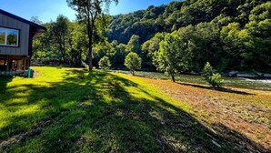 Een huis met een gazon, bomen en een rivier op de achtergrond.