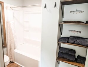 Ein Badezimmer mit einer Badewanne, einer Toilette und einem Regal mit Handtüchern und Fischabbildungen.
