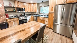 Een keuken met houten kastjes, een roestvrijstalen koelkast, een houten eettafel en een bakstenen muur.