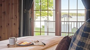 Ein Bett mit Frühstücksangeboten, ein Fenster mit Blick auf ein Haus und Wasser, und eine Holzwand.