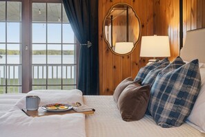 Een hotelkamer met een bed, een ontbijt aan een eettafel, uitzicht op een meer en een spiegel aan de muur.