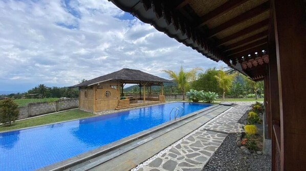 A swimming pool with a wooden structure, stone pathway, and tropical vegetation. - Katah Montana Villa (Jawa Tengah)
