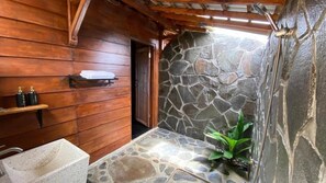 A stone-walled bathroom with a wooden interior, a shower area, and a small shelf with toiletries. - Katah Montana Villa (Jawa Tengah)