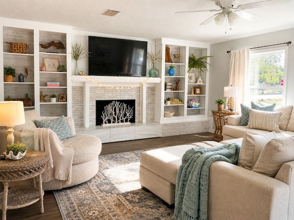 A living room with a fireplace, television, and built-in shelving with decorative items. - Private Pool Near Okaloosa Island+Destin+Navarre. Sunny Days Beach Escape (Mary Esther)