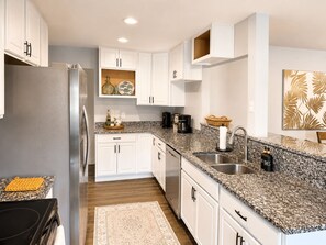 A modern kitchen with white cabinets, granite countertops, a stainless steel refrigerator, and a coffee maker. - Private Pool Near Okaloosa Island+Destin+Navarre. Sunny Days Beach Escape (Mary Esther)