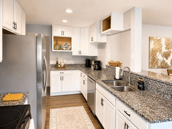 Eine moderne Küche mit weißen Schränken, Granit Arbeitsplatten, einem Edelstahlkühlschrank und einer Kaffeemaschine.