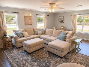 Ein Wohnzimmer mit Ecksofa, Hocker und Deckenventilator.