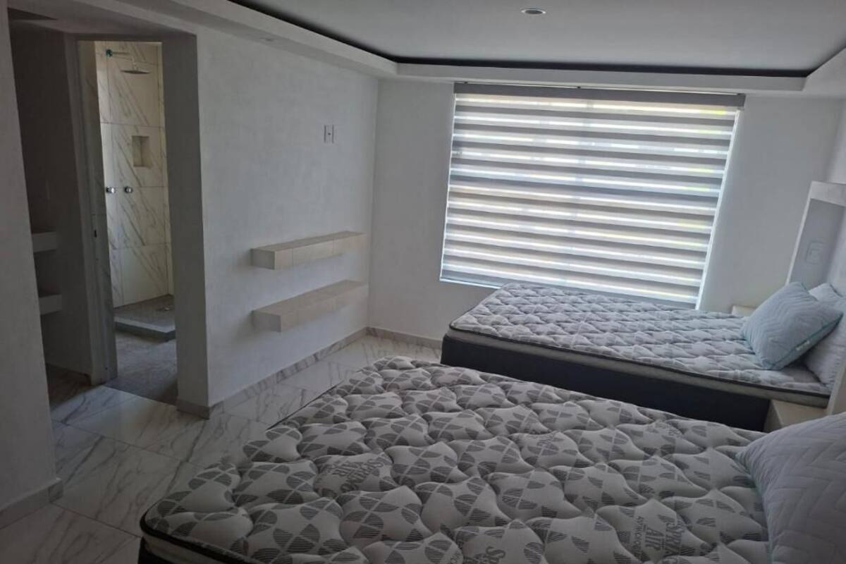Un dormitorio con dos camas, un banco empotrado y una ventana con persianas.