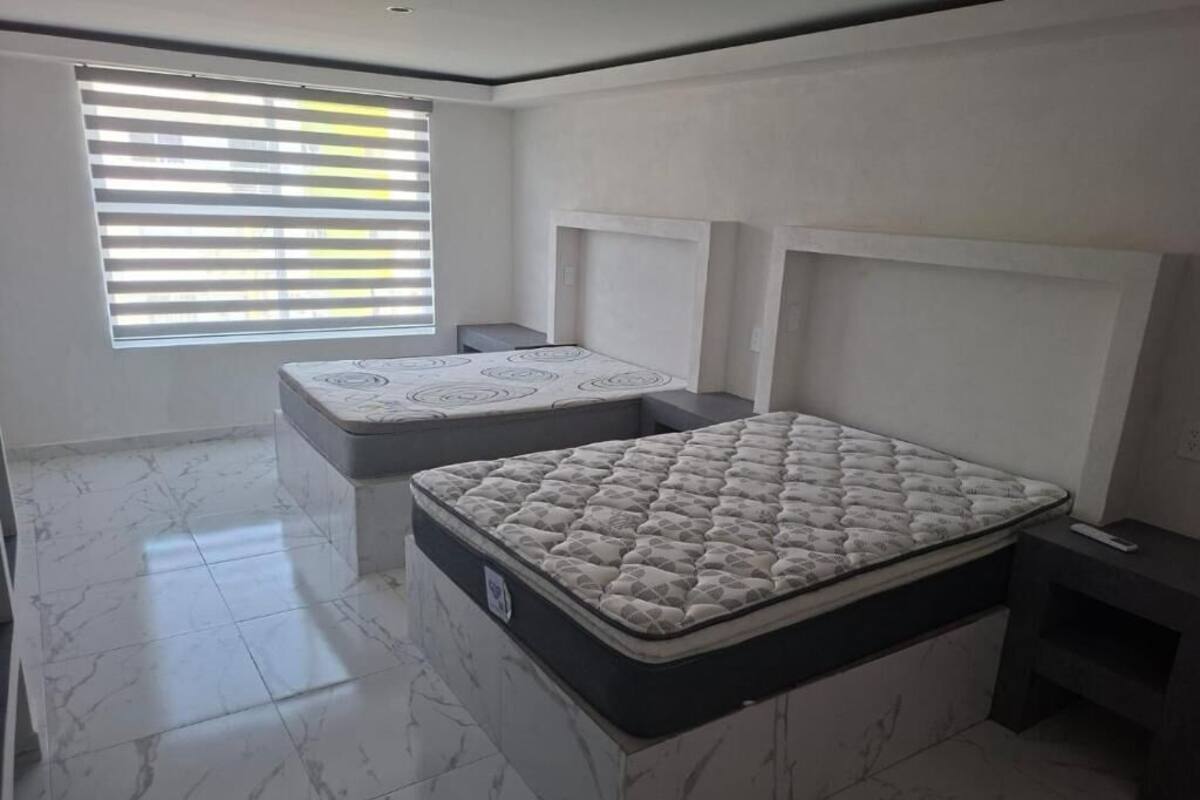 Un dormitorio con dos colchones, una ventana con persianas y suelo de mármol.