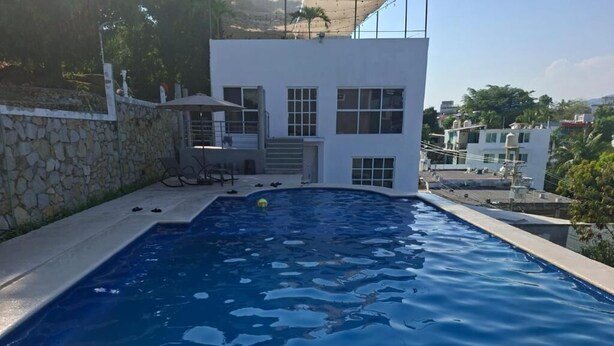 En swimmingpool med en mur av sten, en vit byggnad med fönster och utsikt över andra byggnader.