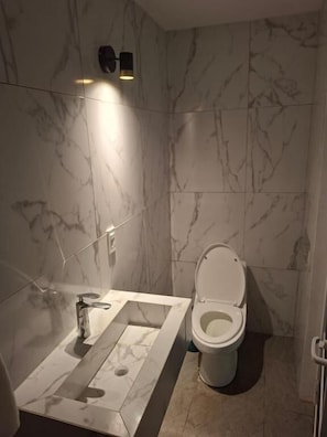 Un baño con lavamanos, inodoro e iluminación de pared.