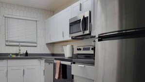 Une cuisine moderne dotée d’appareils électroménagers en acier inoxydable, de meubles blancs et d’un plancher en bois.