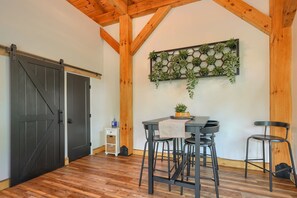 Um quarto com teto de madeira, uma porta de celeiro deslizante, um vaso hexagonal fixado na parede com plantas, uma mesa com dois bancos altos e um pequeno armário branco com uma garrafa azul.