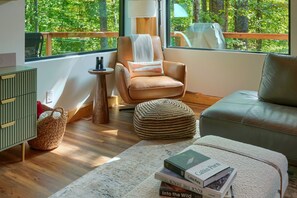 Ein gemütliches Wohnzimmer mit Ledersessel, grünem Sofa, gewebtem Hocker und einer Büchtel Bücher.