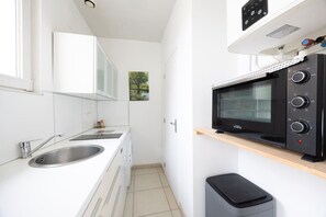 Uma cozinha compacta com pia, micro-ondas e lixeira.