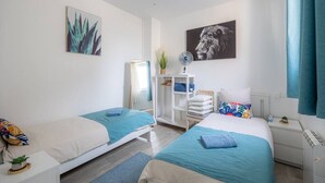 A modern bedroom with two beds, a white wardrobe, a desk, and a wall-mounted fan. - Blue House - Parking - Downtown (Reims)
