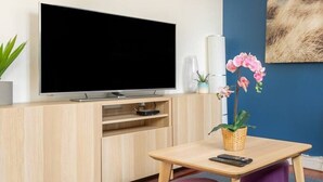 A modern living room with a flat-screen TV, wooden furniture, a blue accent wall, a chandelier, and a painting. - Blue House - Parking - Downtown (Reims)