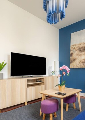Una sala de estar moderna con televisor de pantalla plana, muebles de madera, una pared de acento azul, una araña y un cuadro.
