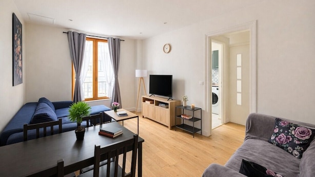 A modern living room with a sofa, a dining table, a TV, and a small side table. - Charming 2-Bedroom Apartment in Downtown - Cozy Houses (Reims)