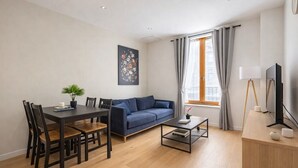 A modern living room with a dining table, sofa, and a TV. - Charming 2-Bedroom Apartment in Downtown - Cozy Houses (Reims)