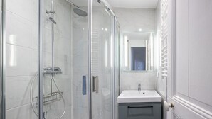 A modern bathroom with a glass-enclosed shower, a white sink, and a mirror above the sink. - Charming 2-Bedroom Apartment in Downtown - Cozy Houses (Reims)