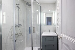 Une salle de bain moderne avec une douche à parois de verre, un lavabo blanc et un miroir au-dessus du lavabo.