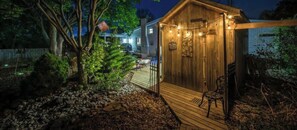 A wooden cabin with a deck, surrounded by trees and a stone pathway.