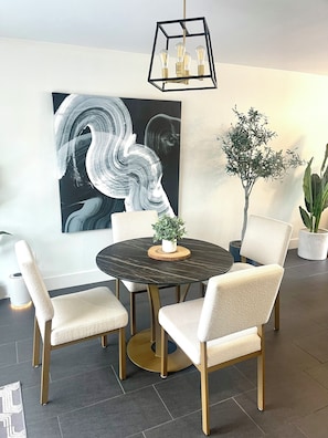 A dining area with a round table, four chairs, a potted plant, and a modern pendant light.