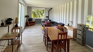 A spacious room with a wooden dining table, chairs, a sofa, and a large window.