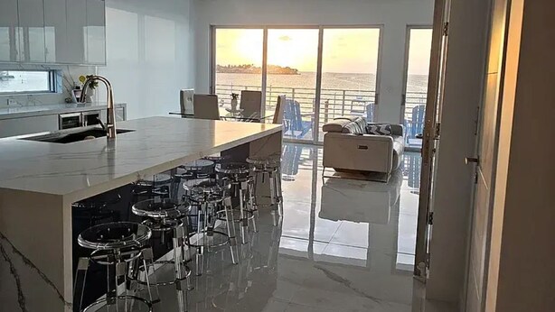 Una cocina moderna con una isla grande, taburetes de bar y vistas al mar a través de amplios ventanales.