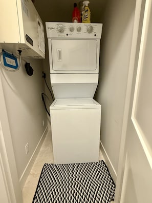 Ein kleiner Waschraum mit einer Waschmaschine und einem Trockner, einer kleinen Ablage für Reinigungsmittel und einer gemusterten Matte auf dem Boden.