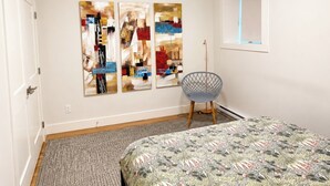 A bedroom with a bed, a chair, and abstract wall art. - Modern Lower Mission Retreat | Luxury Comfort Near Beaches & Wineries (Kelowna)