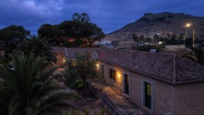 Um edifício rústico com telhado de azulejos, um caminho de pedra e uma montanha ao fundo.
