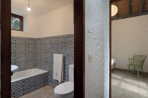 Ein Badezimmer mit gemusterten Fliesen, einer Badewanne, einer Toilette und einem grünen Stuhl.