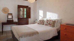 Quarto com teto de madeira, cama com almofadas florais, cómoda de madeira e escrivaninha com espelho.