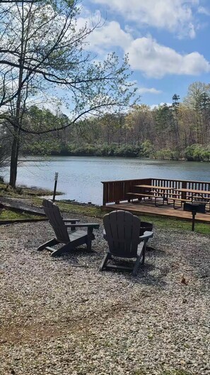 A lakeside picnic area with Adirondack chairs and a wooden deck overlooking the water.