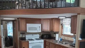 A compact kitchen with a stove, microwave, and sink, wooden cabinets, and a dining area with chairs. - Tiny Home-Cabin near Helen Ga.Lake/Beach/Pools/Playgrounds/Diner/Putt Putt/Sauna (Cleveland)