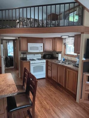 A compact kitchen with a stove, microwave, and sink, wooden cabinets, and a dining area with chairs. - Tiny Home-Cabin near Helen Ga.Lake/Beach/Pools/Playgrounds/Diner/Putt Putt/Sauna (Cleveland)