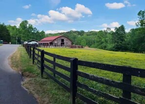 A rural landscape with a barn, a fenced field, and a road.