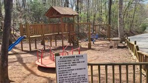 A playground with a wooden structure, including a slide and swings, surrounded by trees. - Tiny Home-Cabin near Helen Ga.Lake/Beach/Pools/Playgrounds/Diner/Putt Putt/Sauna (Cleveland)