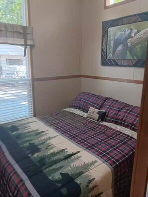 A bedroom with a bed, a window with blinds, a painting on the wall, and a door. - Tiny Home-Cabin near Helen Ga.Lake/Beach/Pools/Playgrounds/Diner/Putt Putt/Sauna (Cleveland)